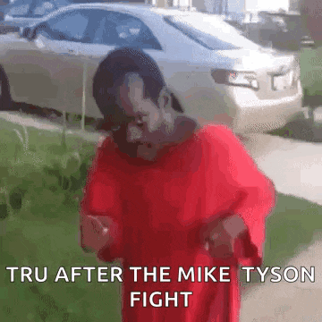 a man in a red shirt is standing in front of a car .