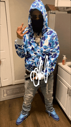 a man wearing a blue camo hoodie stands in front of a kitchen counter