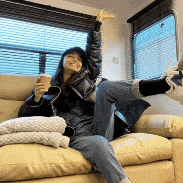 a woman is sitting on a couch with her arms in the air holding a cup of coffee