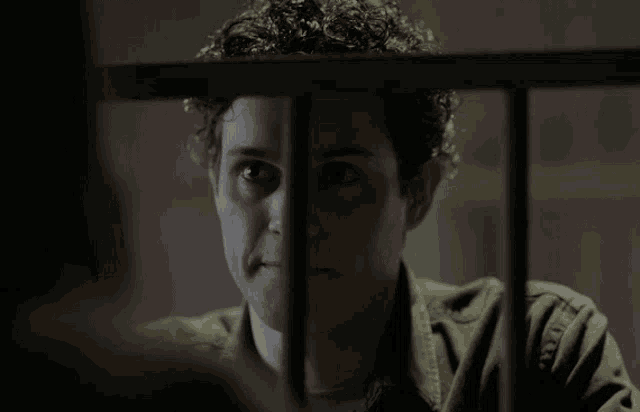 a man with curly hair behind bars looking at the camera