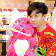 a man in a red shirt is holding a pink stuffed animal in front of a fountain