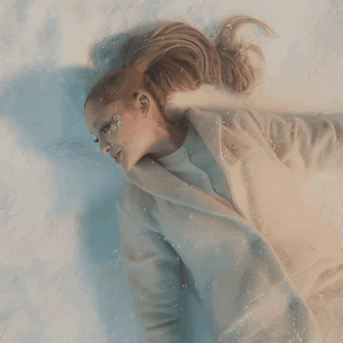 a woman in a white coat laying in the snow