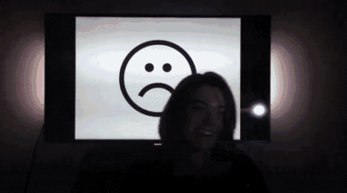 a woman is smiling in front of a sad face on a tv screen