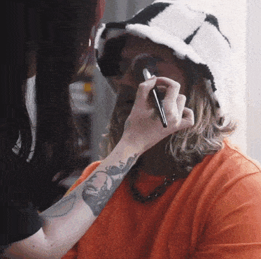 a woman is applying makeup to a man wearing a bucket hat