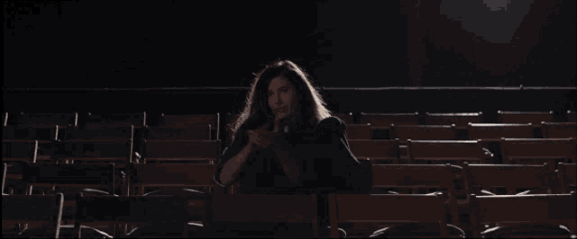 a woman is sitting in a dark auditorium with her arms in the air