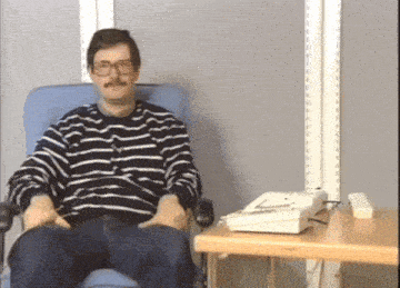 a man wearing glasses and a striped shirt sits in a chair