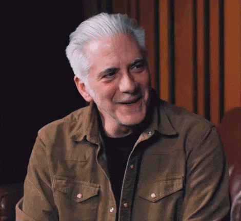 a man in a brown shirt is smiling and the word okay is on the screen