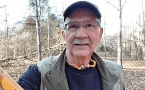 a man wearing glasses and a hat is standing in the woods .