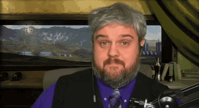 a man with a beard wearing a purple shirt and a black vest