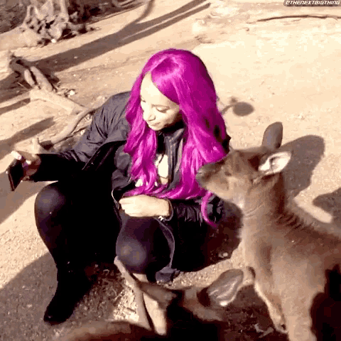 a woman with purple hair is sitting next to a kangaroo and taking a picture