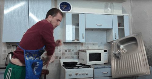 a man in an apron is standing in a kitchen with a clock on the wall that reads 7:30