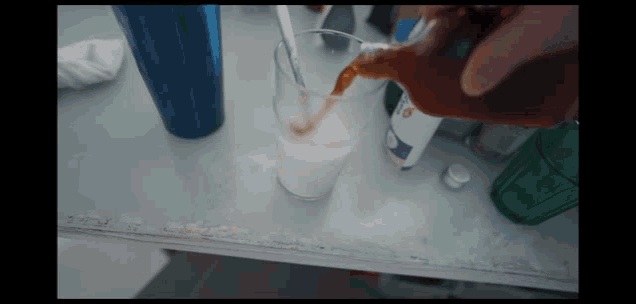 a person pouring a drink into a glass with a spoon in it
