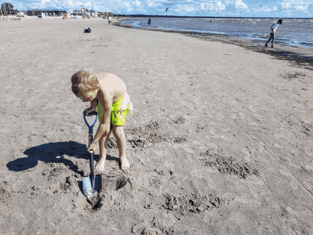 a boy digging in the sand with a shovel