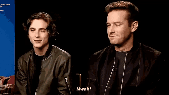 two men are sitting next to each other in front of a microphone and one of them is making a funny face .