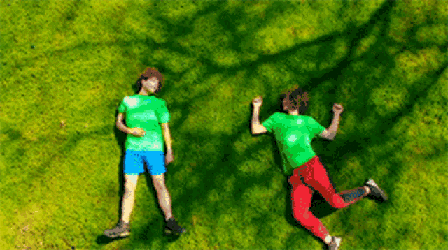 two boys laying on the grass with their shadows on the grass