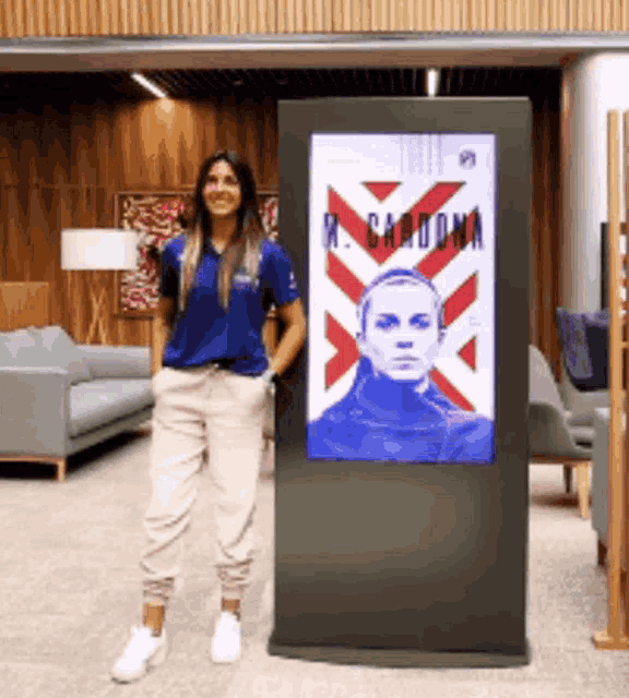 a woman in a blue shirt stands in front of a large screen that says m. cardona