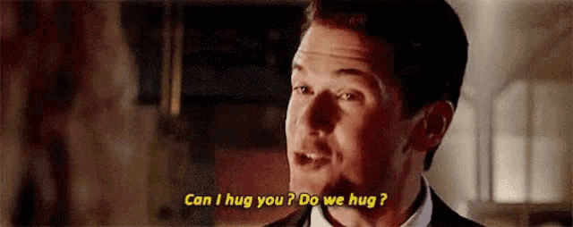 a man in a suit and tie is talking to another man and asking him if he can hug him .