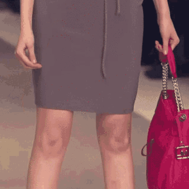 a woman in a grey skirt holds a red purse