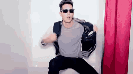 a man wearing sunglasses and a jacket is dancing in a room .