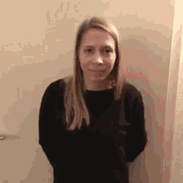 a woman in a black sweater is standing in front of a wall