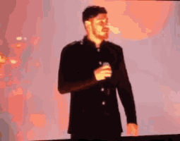 a man singing into a microphone in front of a red background