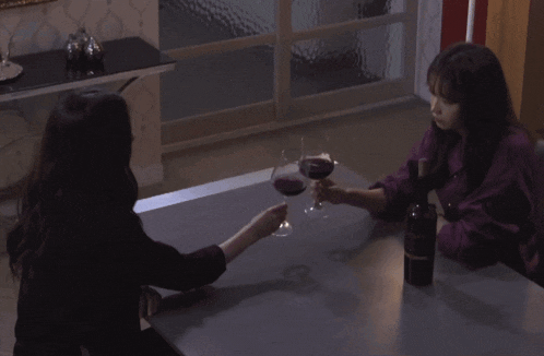 two women are sitting at a table drinking wine