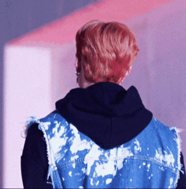 a person with red hair wearing a black hoodie and a blue vest