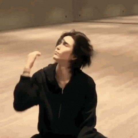 a man in a black hoodie is sitting on the floor in a room and making a funny face .