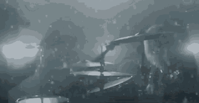 a man is playing drums in a dark room while a woman sings into a microphone .