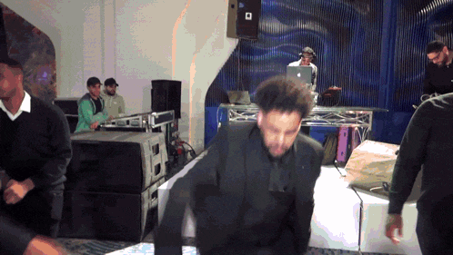 a man in a suit is dancing in a room with a dj behind him