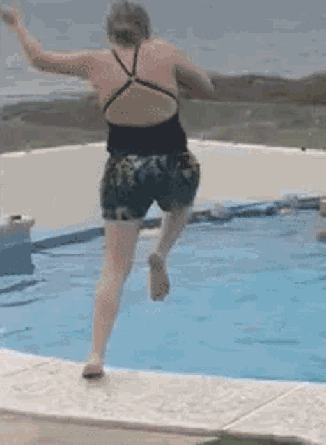 a woman in a black tank top and shorts is jumping into a swimming pool