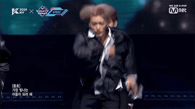 a man in a black jacket is performing on a stage in front of a screen that says we are k pop