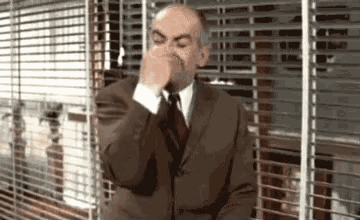 a bald man in a suit and tie is covering his nose with his hand .
