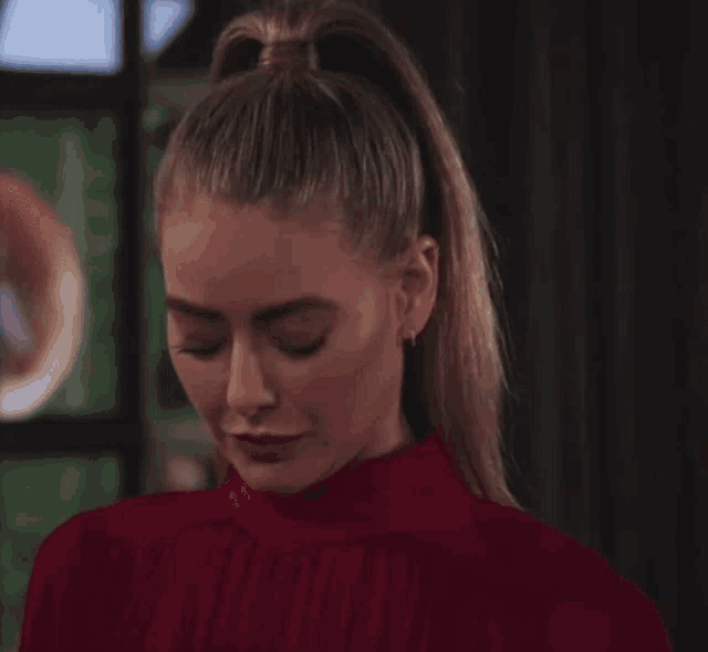 a woman with a ponytail is wearing a red top and earrings
