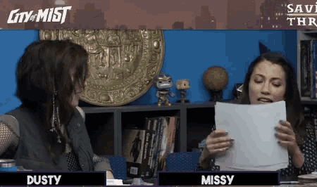 two women are sitting at a table reading a piece of paper with the name missy on it