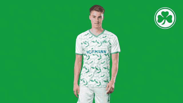 a man wearing a hofmann shirt and shorts stands in front of a green background