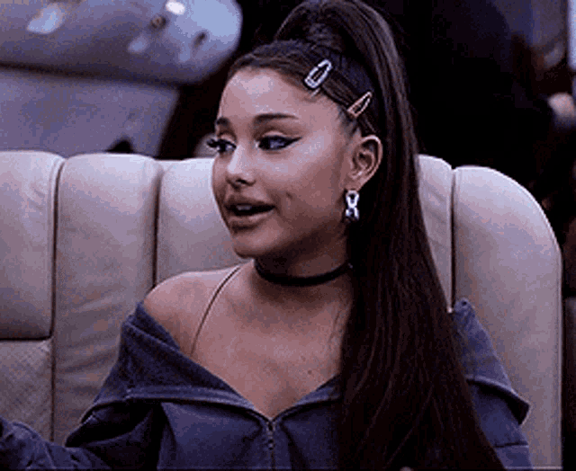 ariana grande is wearing a choker and earrings while sitting on a chair .