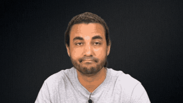 a man with a beard is wearing a grey shirt with a microphone attached to it