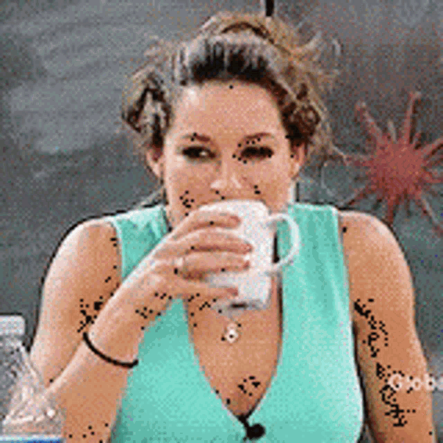 a woman in a blue tank top is drinking from a white cup