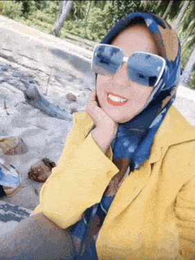 a woman wearing sunglasses and a scarf smiles for a picture