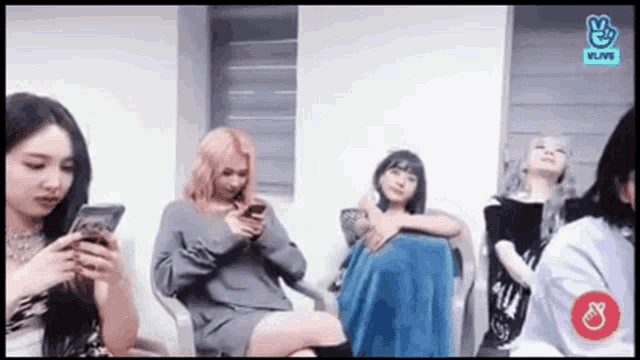 a group of young women are sitting in chairs looking at their phones .