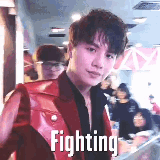 a man in a red jacket is standing in front of a crowd with the word fighting above him