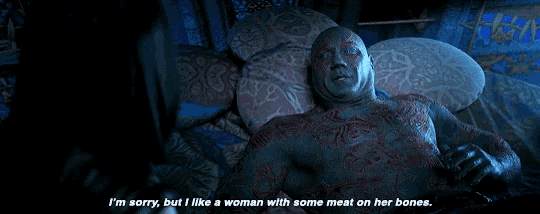 a man with a lot of tattoos is laying on a bed with a woman with some meat on her bones