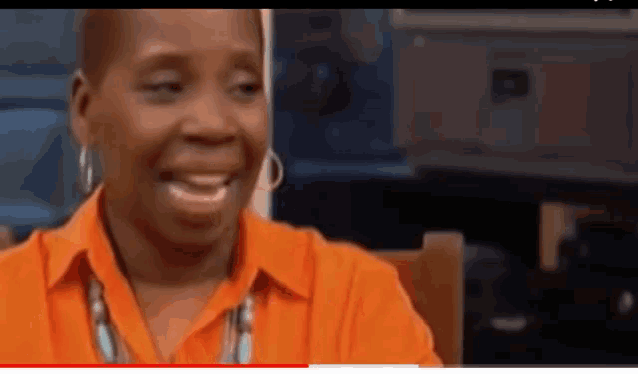 a woman wearing an orange shirt and earrings is smiling .