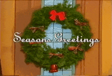 a christmas wreath hangs on a door with the words seasons greetings below it