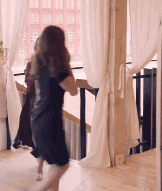 a woman in a black dress stands in front of a window with white curtains
