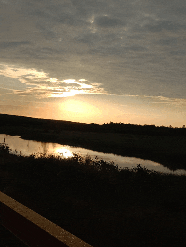 the sun is setting over a body of water with trees in the background