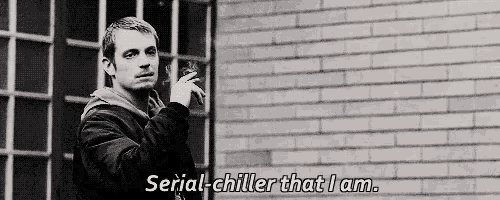a man is smoking a cigarette in front of a brick wall and says serial chiller that i am .