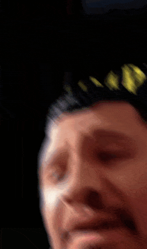a close up of a man 's face with a black background and a few yellow lights