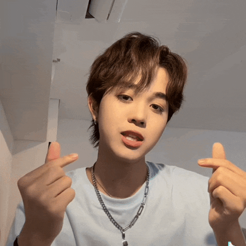 a young man wearing a blue shirt and a chain necklace is giving a thumbs up